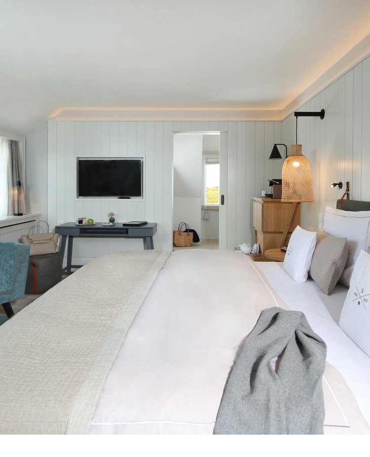 Landhaus-Zimmer im Hotel auf Sylt Helles Hotelzimmer mit Doppelbett, Sessel, Schreibtisch und TV. Moderne, gemütliche Einrichtung mit sanften Farben.