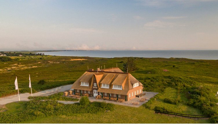 Reetgedecktes Hotel in grüner Landschaft mit Meerblick, Terrasse und Flaggen, Landhaus Severin*s Morsum Kliff, Sylt.