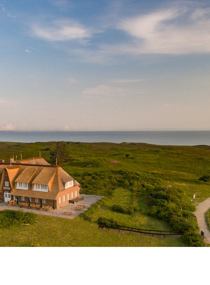 Reetgedecktes Hotel Landhaus Severin*s auf Sylt, umgeben von grüner Landschaft, mit Blick auf das Meer.