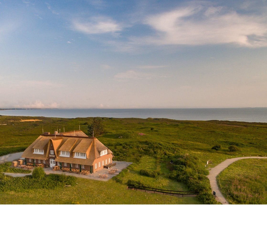 Luftaufnahme Landhaus Severin*s Reetgedecktes Hotel Landhaus Severin*s auf Sylt, umgeben von grüner Landschaft, mit Blick auf das Meer.