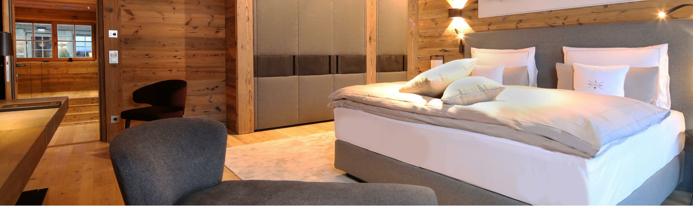 Gemütliches Hotelzimmer mit Holzwänden, großem Bett, grauem Sessel und moderner Kunst an der Wand im Severin*s Lech.