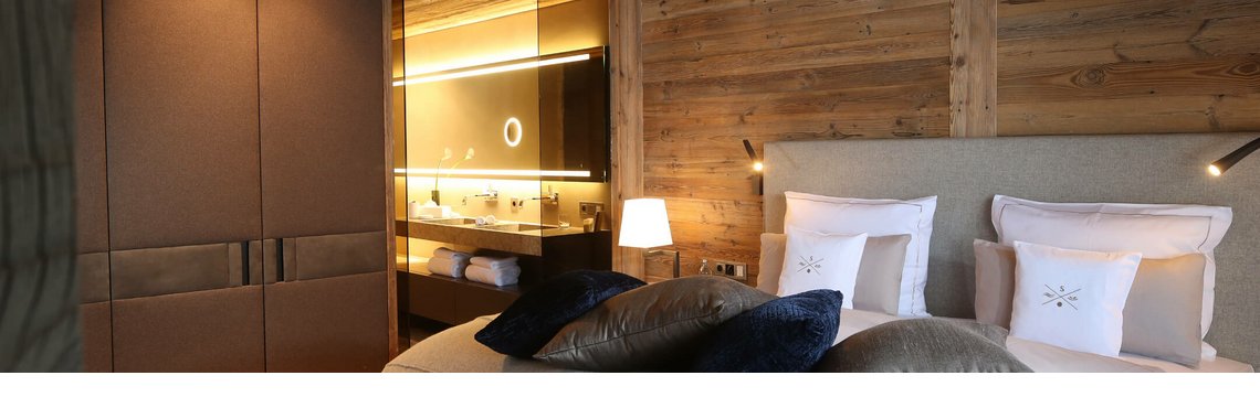 Luxuriöses Hotelzimmer mit Holzwänden, gemütlichem Bett, eleganter Beleuchtung und Blick ins moderne Badezimmer.