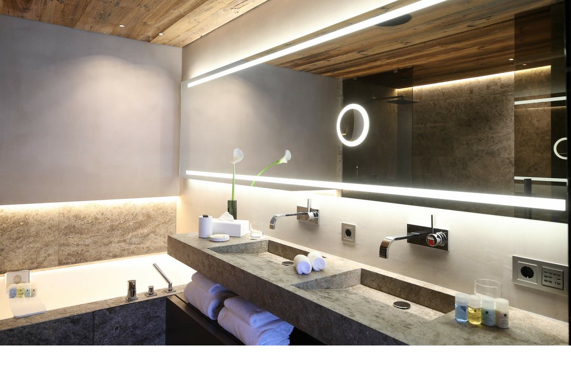 Modernes Badezimmer mit Steinwaschbecken, großer Spiegel, Badewanne und Holzdecke im Severin*s The Alpine Retreat, Lech.