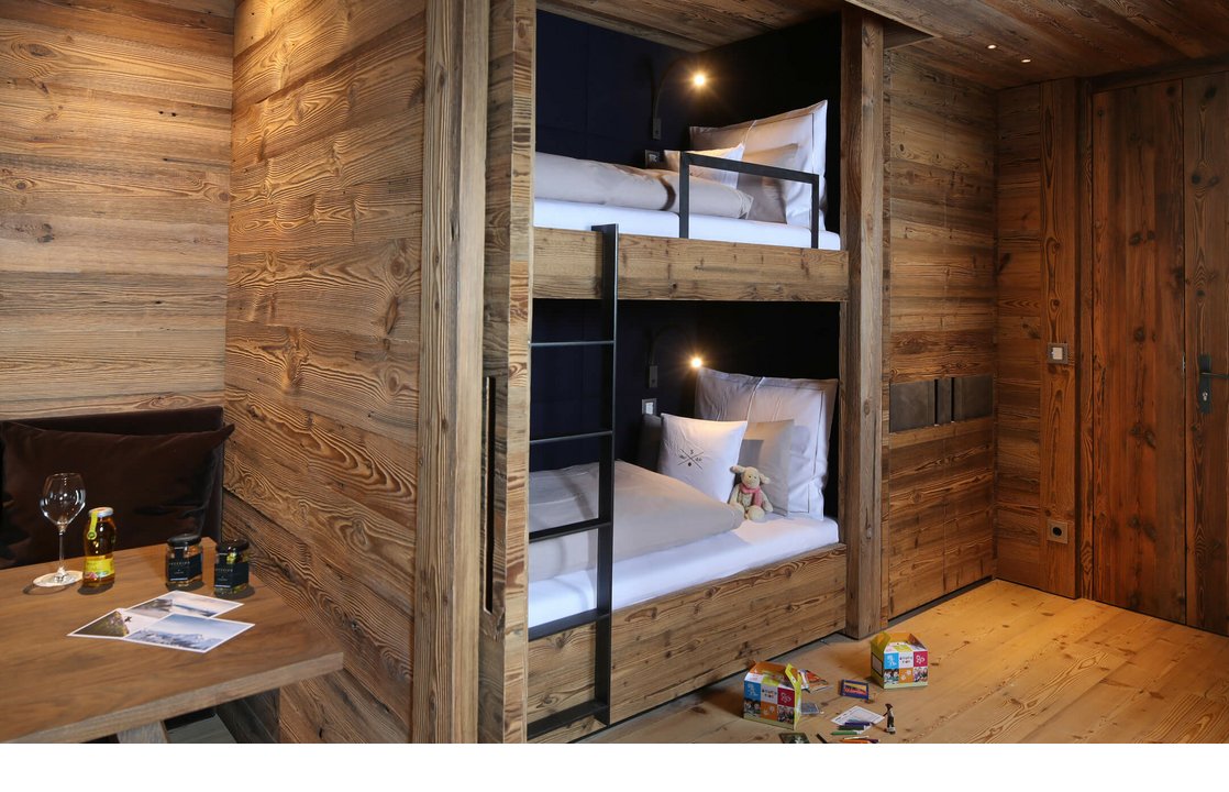 Gemütliches Zimmer mit Etagenbett aus Holz, Tisch mit Getränken und Spielzeug auf dem Boden im Severin*s The Alpine Retreat.