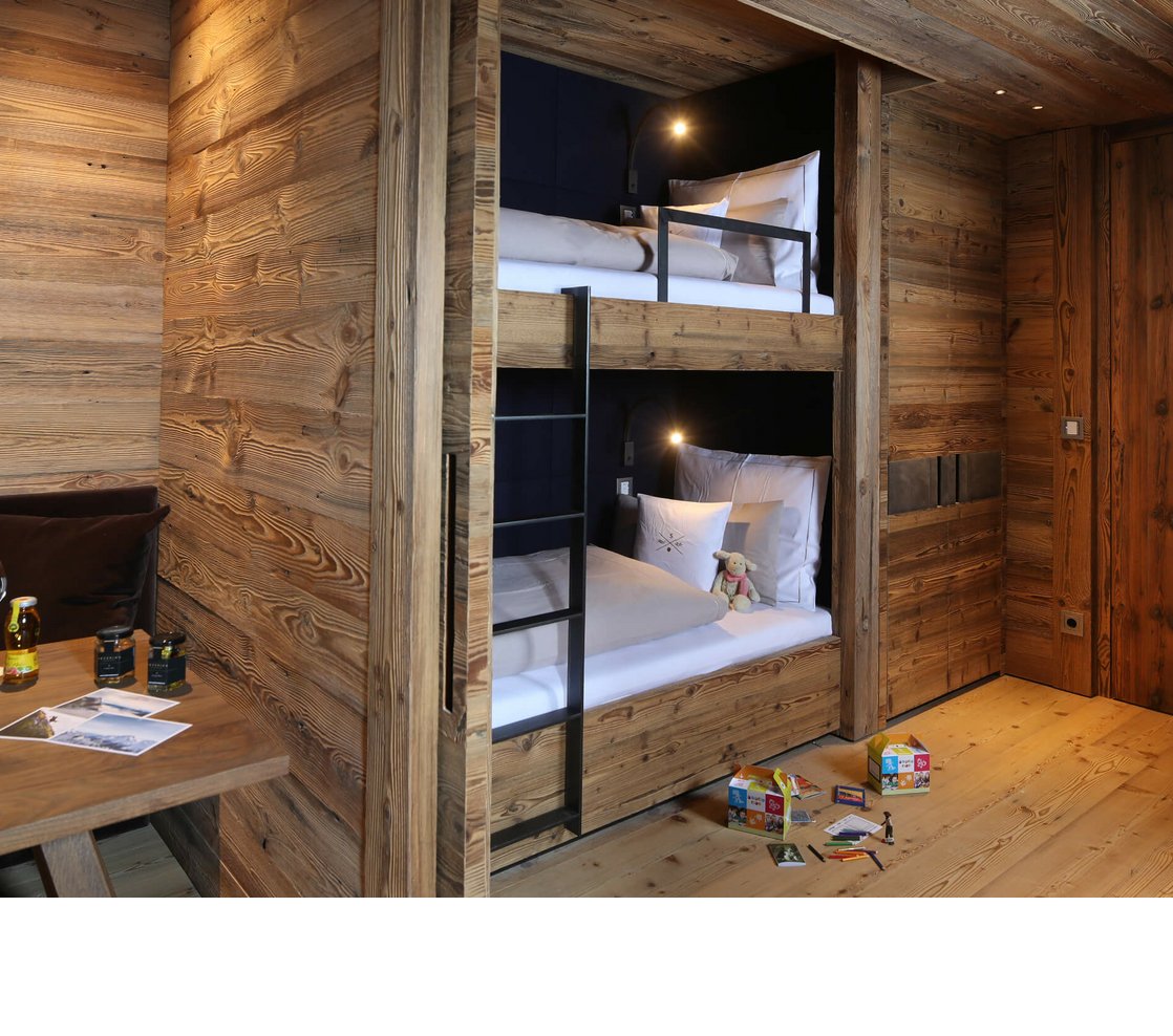 Etagenbett für 2 Kinder in der Famly Suite im Severin*s – The Alpine Retreat Gemütliches Zimmer mit Etagenbett aus Holz, Tisch mit Getränken und Spielzeug auf dem Boden im Severin*s The Alpine Retreat.