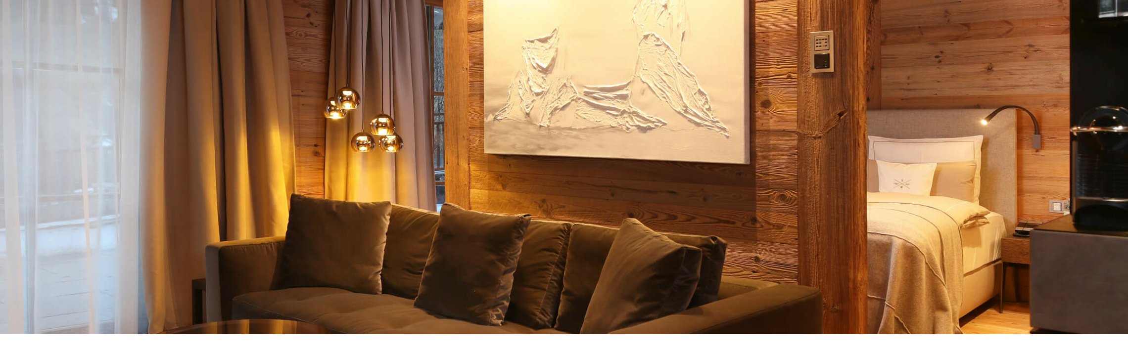 Gemütliches Hotelzimmer mit Holzverkleidung, Sofa, Kunstwerk, Bett und eleganter Beleuchtung im Severin*s The Alpine Retreat.
