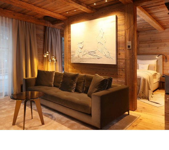 Wohnbereich der Junior Suite im Severin*s – The Alpine Retreat Gemütliches Hotelzimmer mit Holzverkleidung, Sofa, Kunstwerk, Bett und eleganter Beleuchtung im Severin*s The Alpine Retreat.