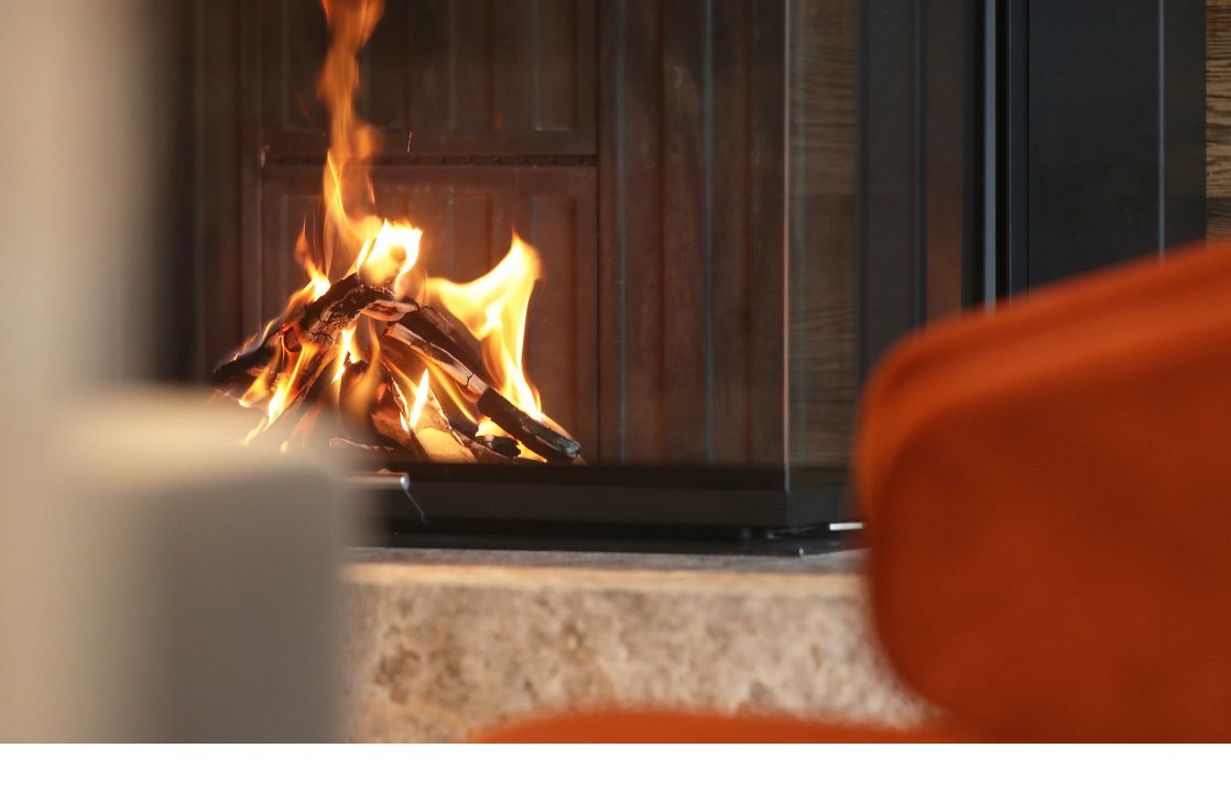 Gemütliches Kaminfeuer im Severin*s The Alpine Retreat, umgeben von warmen, orangefarbenen Sitzgelegenheiten.