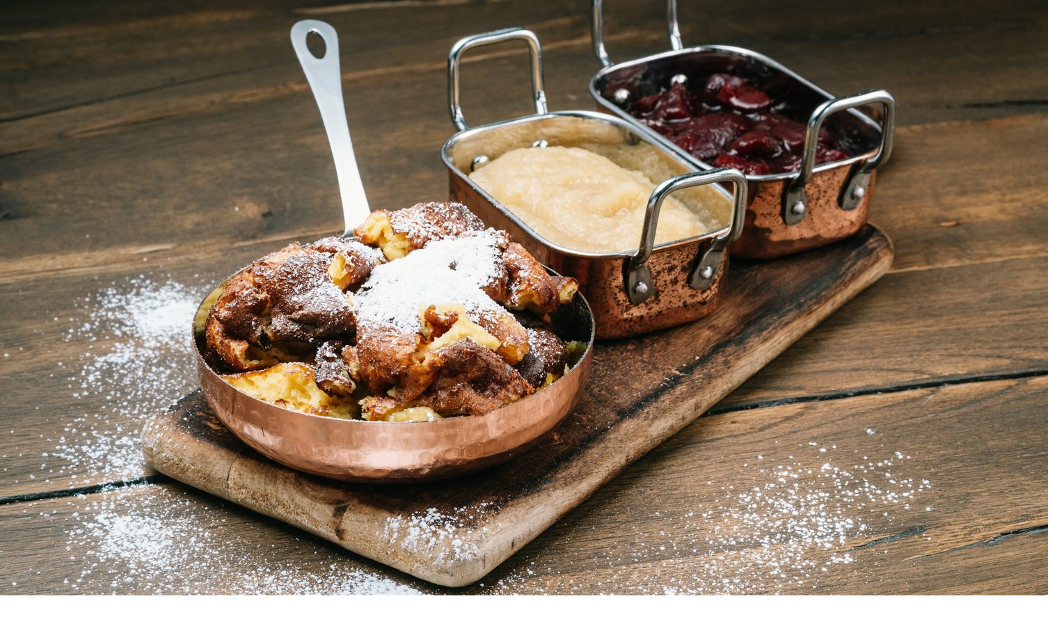 Restaurant im Hotel Severin*s – The Alpine Retreat in Lech Kaiserschmarrn mit Puderzucker, Apfelmus und Zwetschgenröster in Kupferpfannen auf Holzbrett.