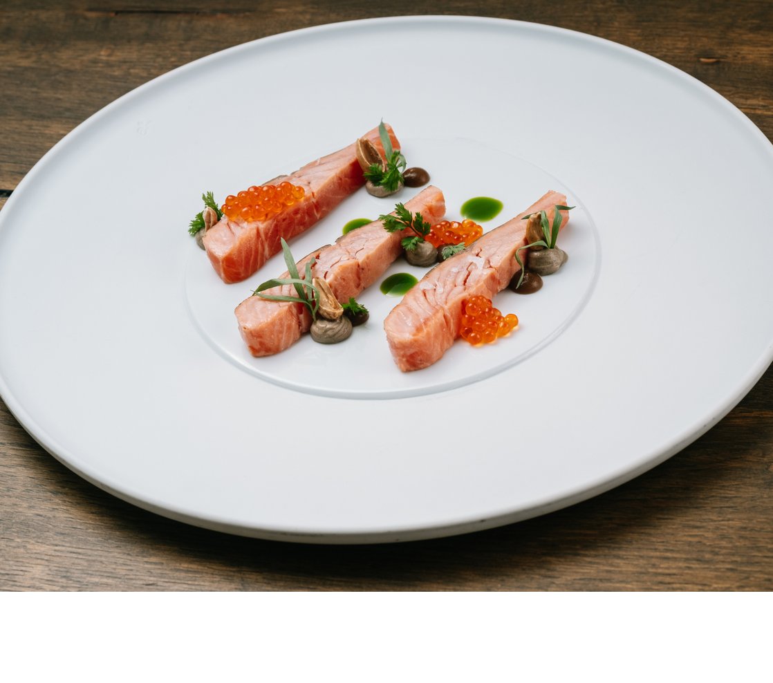 Gourmetgericht mit Lachs, Kaviar und Kräutern kunstvoll auf weißem Teller angerichtet.