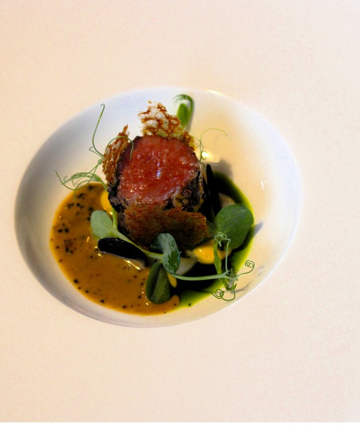 Gourmetgericht auf weißem Teller, kunstvoll angerichtet mit Fleisch, Sauce und Kräutern, im Severin*s The Alpine Retreat.