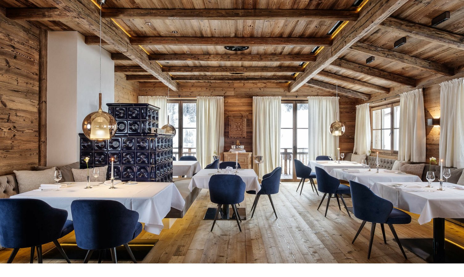 Restaurant im Hotel Severin*s – The Alpine Retreat in Lech Gemütliches Restaurant mit Holzwänden, blauen Samtstühlen, weißen Tischdecken und großen Fenstern mit Bergblick.