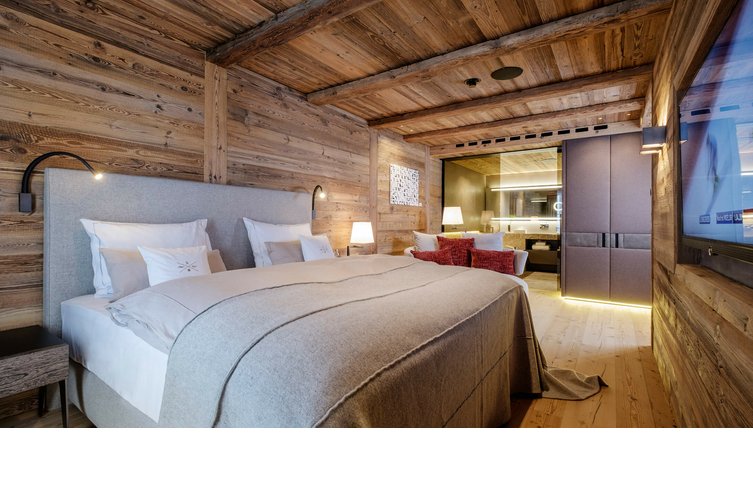 Gemütliches Hotelzimmer mit Holzwänden, großem Bett, moderner Beleuchtung und Blick ins luxuriöse Badezimmer.