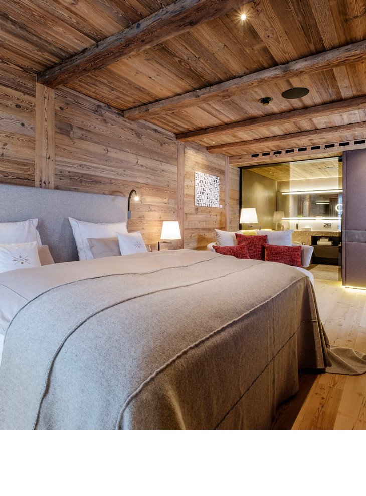 Gemütliches Hotelzimmer mit Holzwänden, großem Bett, moderner Beleuchtung und Blick ins luxuriöse Badezimmer.