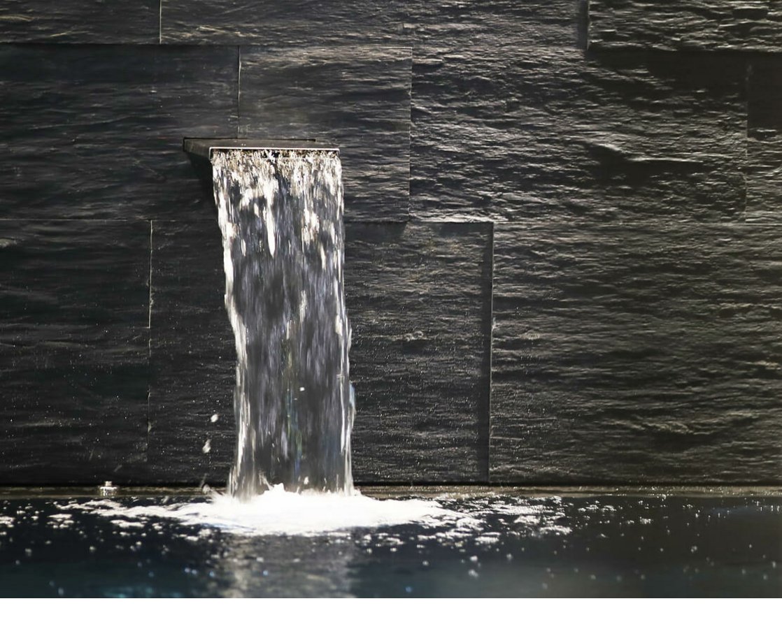 Wasserfall im Wellnessbereich des Severin*s Wasserfall fließt über dunkle Steinwand in einen Pool im Severin*s The Alpine Retreat, Lech.