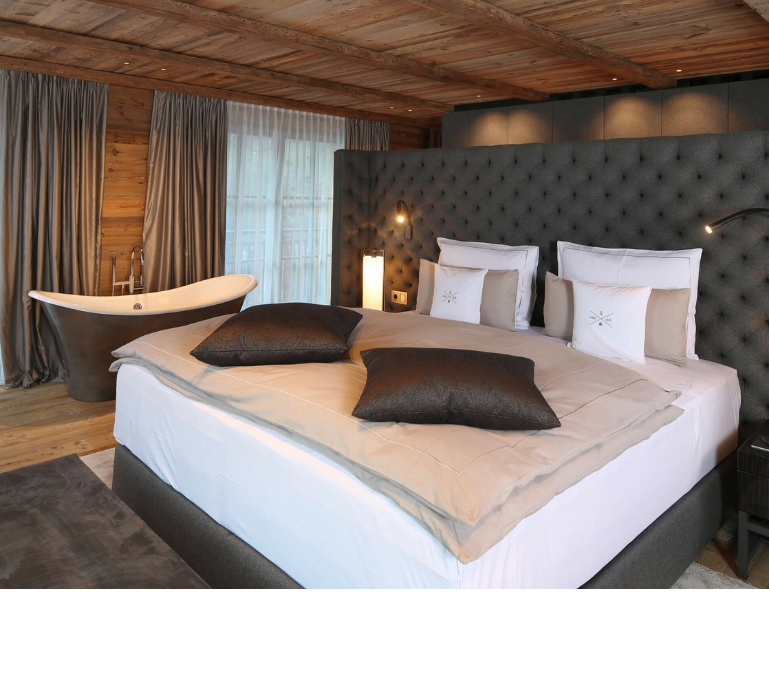 Luxuriöses Hotelzimmer mit großem Bett, freistehender Badewanne und eleganter Holzeinrichtung im Severin*s The Alpine Retreat.