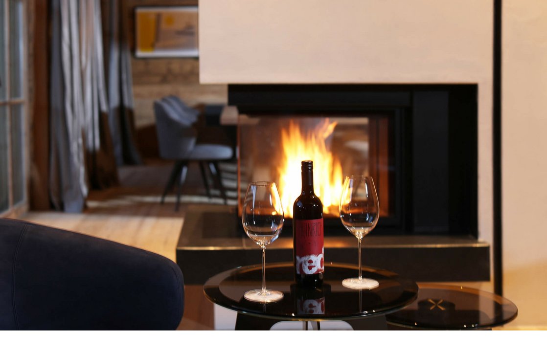 Gemütliche Lounge mit Kamin, Weinflasche und Gläsern auf einem Tisch im Severin*s The Alpine Retreat, Lech.