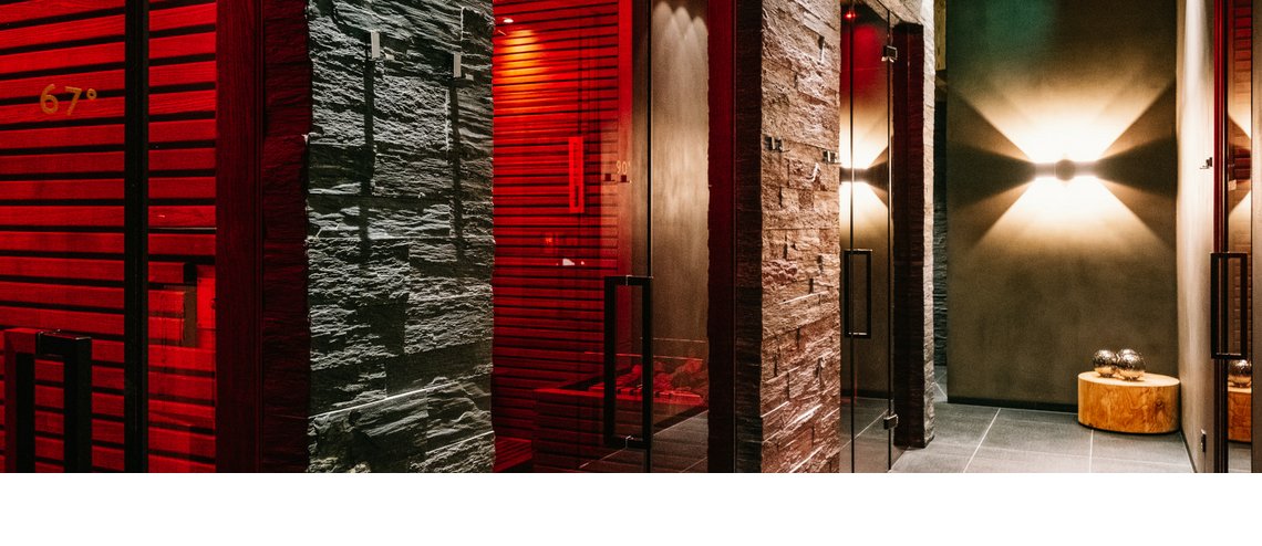 Flur mit moderner Beleuchtung, Steinwänden und Glastüren, die zu Saunen im Hotel Severin*s The Alpine Retreat führen.