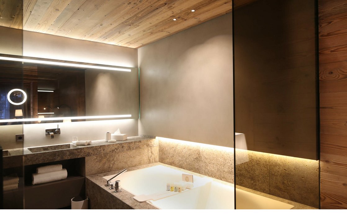 Luxuriöses Badezimmer mit großer, beleuchteter Badewanne, modernem Waschbecken und Holzdecke im Hotel Severin*s, Lech.
