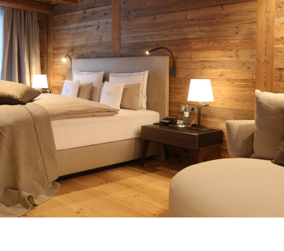Schlafbereich Severin*s – The Alpine Retreat Senior Suite Gemütliches Hotelzimmer mit Holzwänden, großem Bett, eleganten Kissen, Sofa und sanfter Beleuchtung im Severin*s Lech.