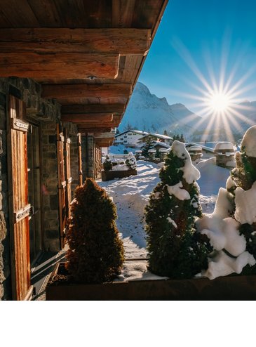 Sonnenaufgang über schneebedeckten Bergen und Hotelterrasse mit Holzelementen und Pflanzen im Hotel Severin*s in Lech.