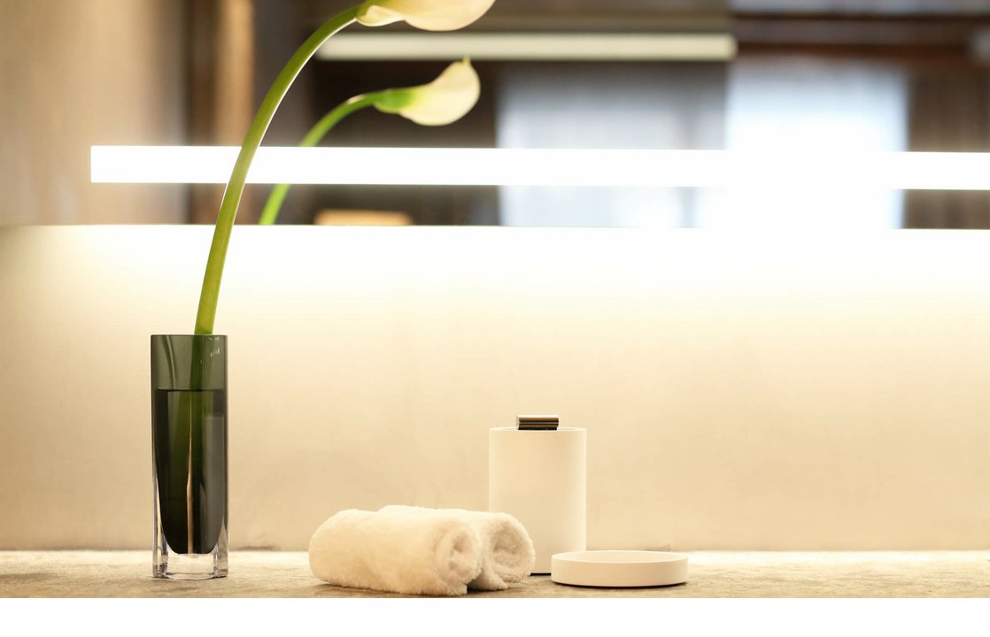 Elegante Baddekoration mit weißen Handtüchern, Vase mit Blumen und stilvollen Accessoires auf Steinablage.