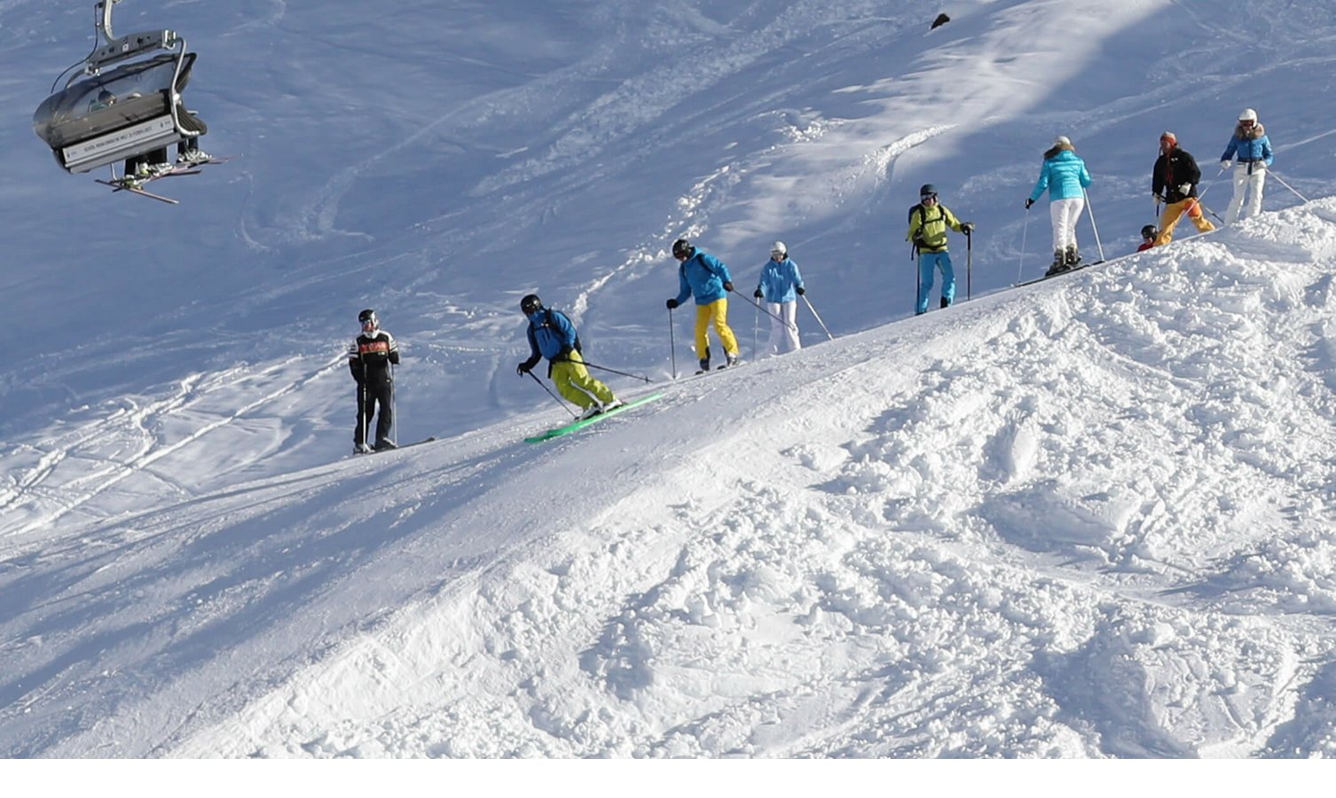 Gruppe von Skifahrern auf verschneiter Piste bei Sonnenschein, Sessellift im Hintergrund.