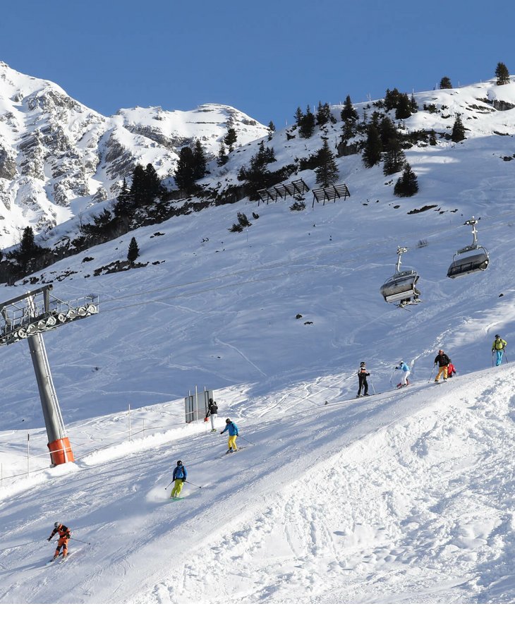Skilift in Lech am Arlberg Skifahrer auf schneebedecktem Hang unter Sessellift, umgeben von verschneiten Bergen und blauem Himmel.