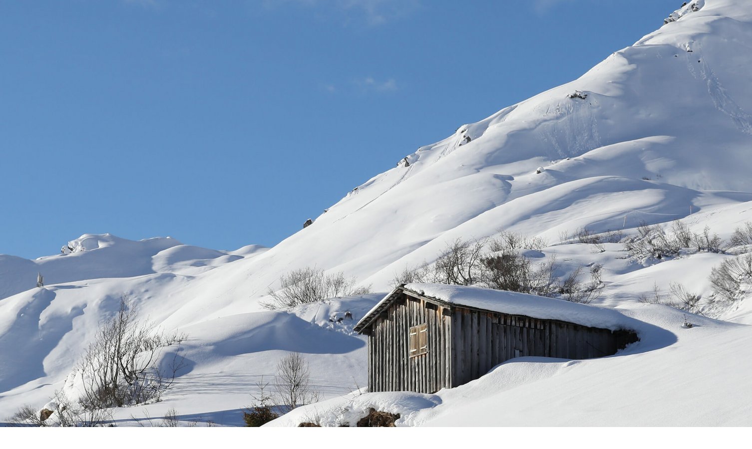 Holzhütte in verschneiter Berglandschaft unter klarem, blauem Himmel.