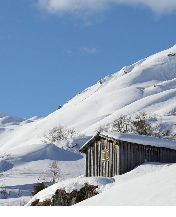 Holzhütte in verschneiter Berglandschaft unter klarem, blauem Himmel.