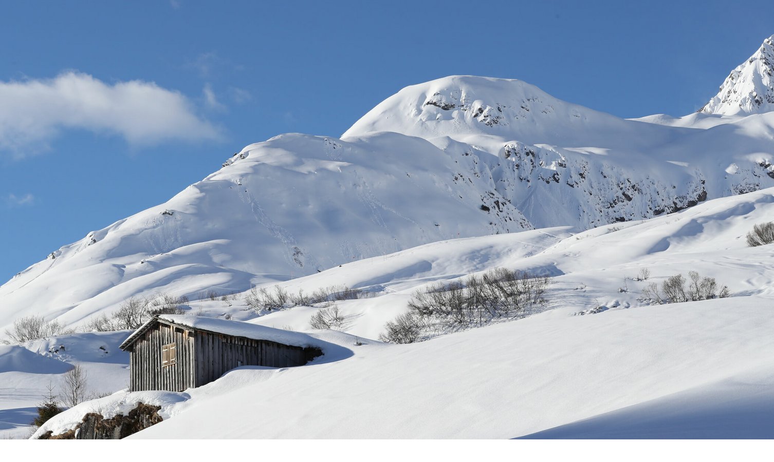 Skigebiet Lech am Arlberg Holzhütte in verschneiter Berglandschaft unter blauem Himmel.