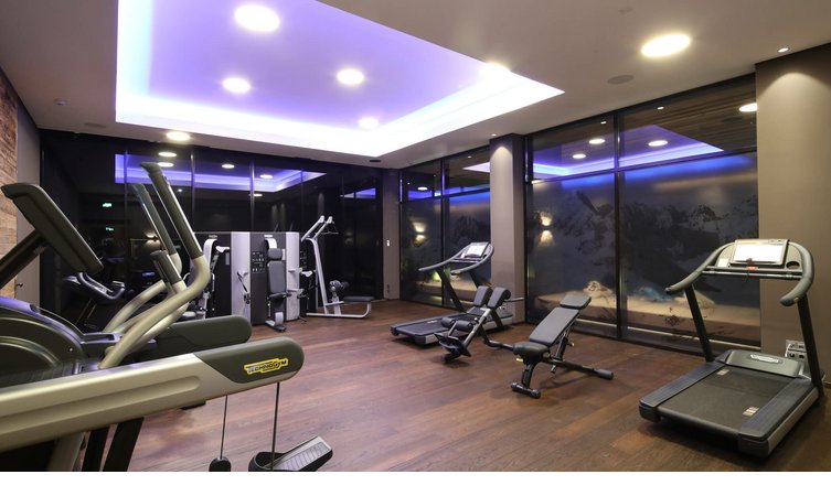 Moderner Fitnessraum im Hotel Severin*s mit Laufbändern, Kraftgeräten und Bergpanorama hinter Glaswand.