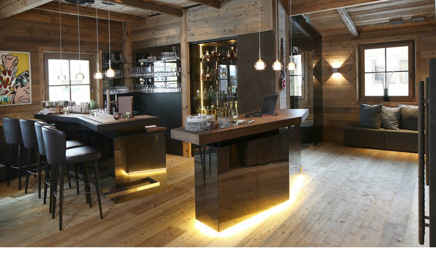 Gemütliche Hotelbar mit Holzwänden, modernen Hockern, beleuchtetem Tresen und dekorativen Elementen im Severin*s Lech.