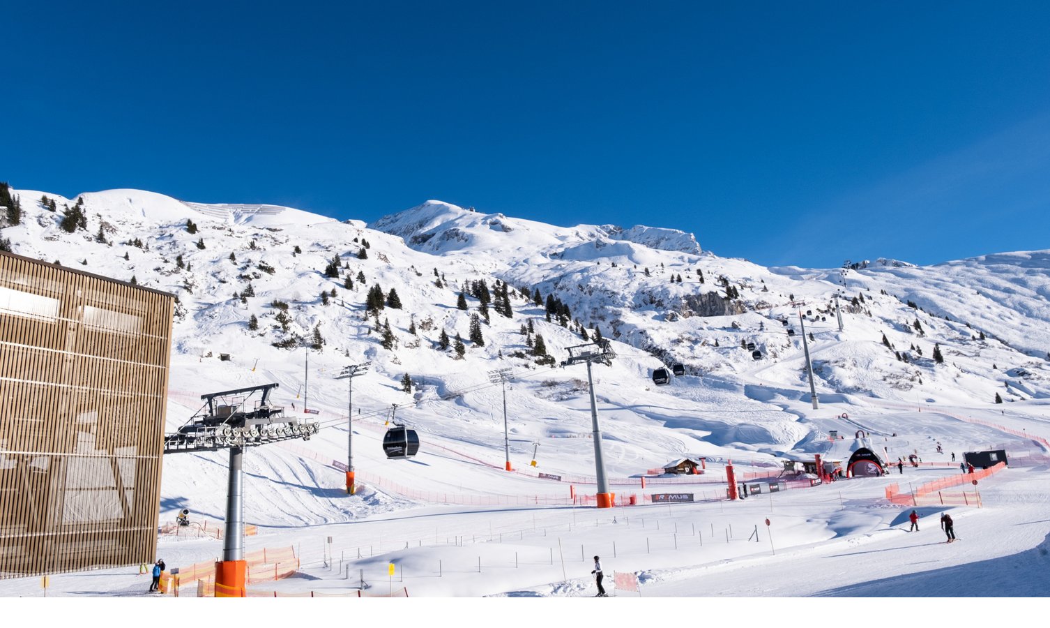 Skifahren in Lech l Hotel Severin*s - The Alpine Retreat Verschneite Skipiste mit Sessellift, Gondeln und Skifahrern vor einem klaren blauen Himmel.