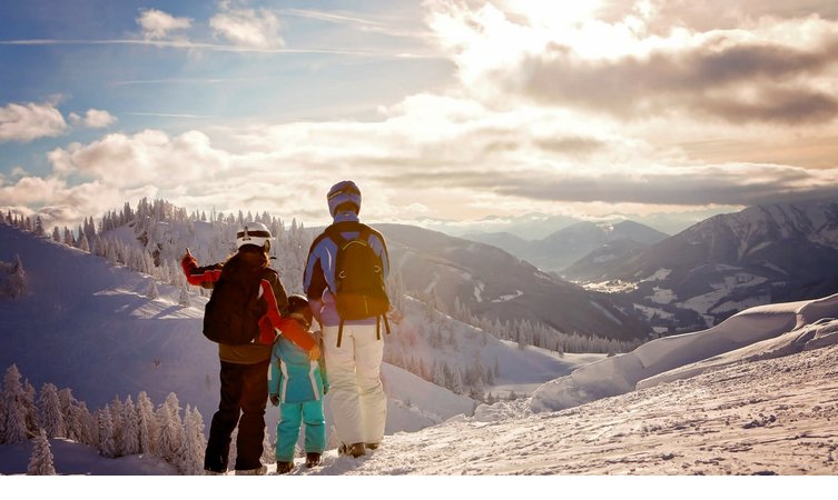Familie in Skiausrüstung genießt winterliche Berglandschaft bei Sonnenuntergang.