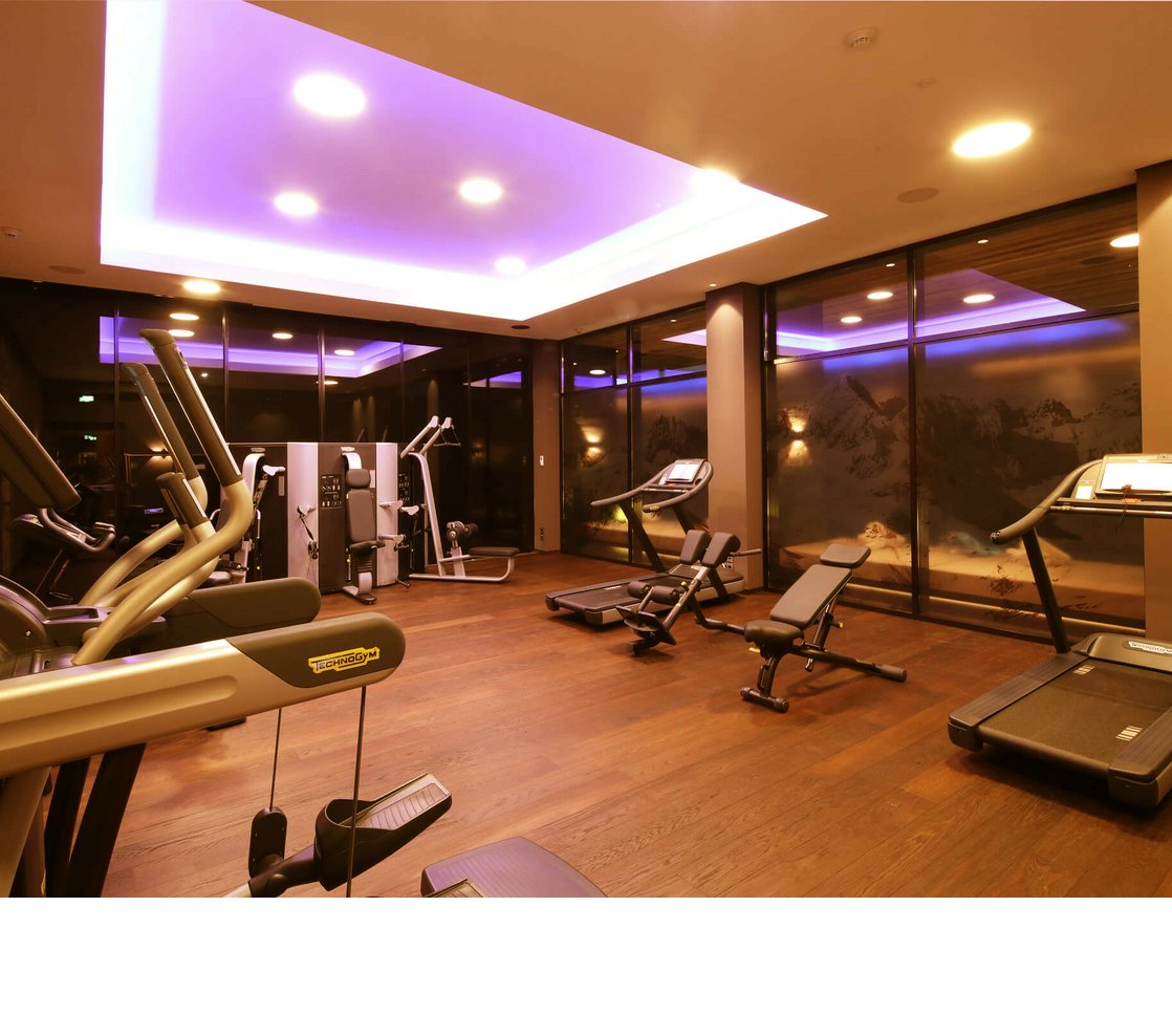 Modernes Fitnessstudio im Hotel Severin*s, Lech, mit Laufbändern, Kraftgeräten und stimmungsvoller Beleuchtung.