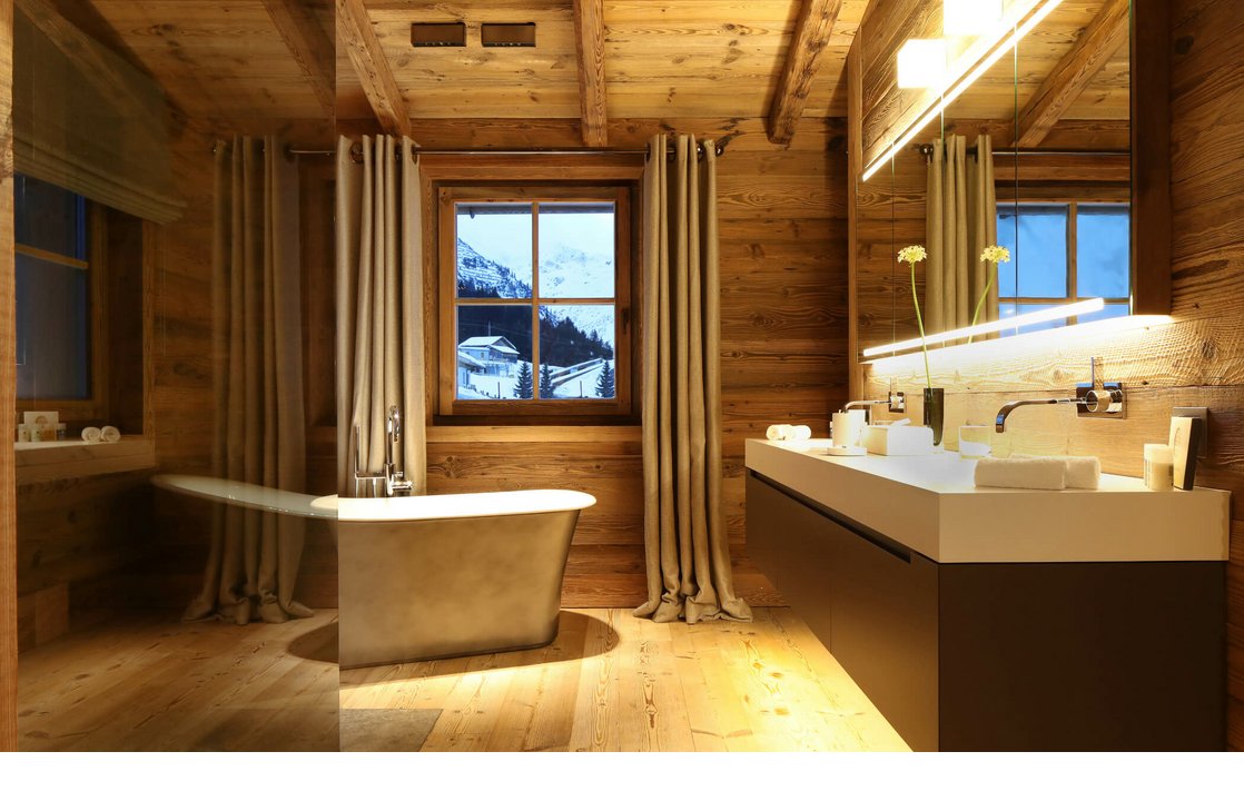 Luxuriöses Hotelbad mit freistehender Wanne, Holzverkleidung und Bergblick durch das Fenster.
