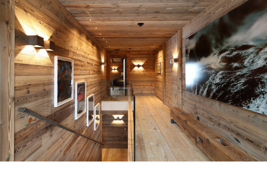Holzverkleideter Hotelflur mit Treppen, modernen Kunstwerken und stimmungsvoller Beleuchtung im Severin*s The Alpine Retreat.