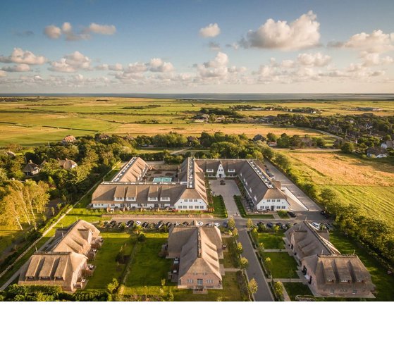 Gelände-Draufsicht auf das Areal des Hotel Severin*s Resort & Spa sowie der Küste Sylts per Drohne Luftaufnahme des Severin*s Resort & Spa auf Sylt, umgeben von grünen Feldern und idyllischer Landschaft.
